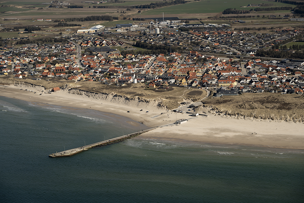 Molen ved Løkken med byen i baggrunden. Billedet er taget fra søsiden, og på billedet ses fiskekuttere der er trukket op på stranden, redningshuset og den centrale bydel